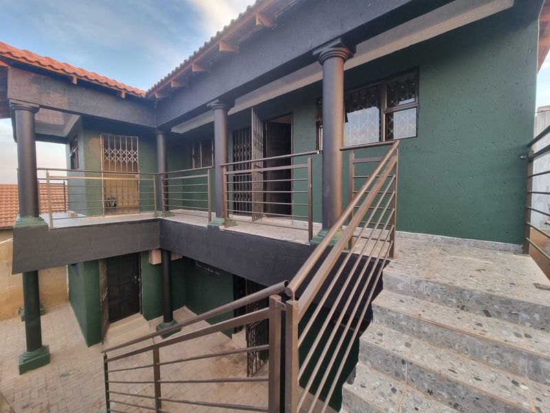 A multi-level exterior view of an apartment building featuring a tiled staircase, metal balustrades, and a paved courtyard area.