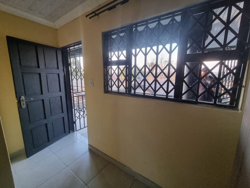 A functional hallway featuring tiled flooring, a secure panel door, and windows fitted with security bars.