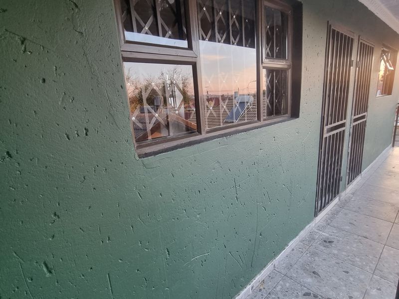 An exterior walkway or balcony area featuring tiled flooring, security gates, and security bars on the windows.