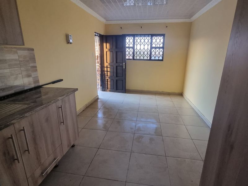 An empty open-plan living and kitchen area featuring tiled floors, built-in cabinetry, and security-fitted doors and windows.