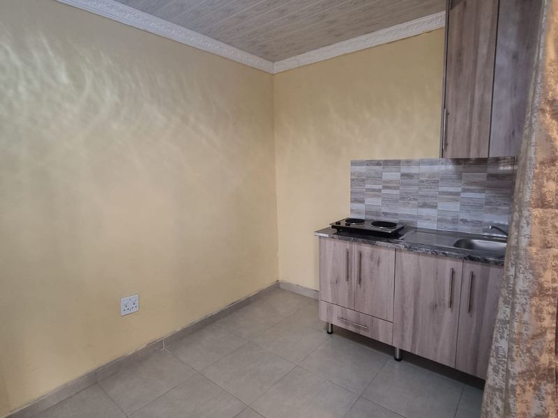 A compact kitchen area featuring built-in cabinetry, a stainless steel sink, an electric cooktop, and tiled flooring.