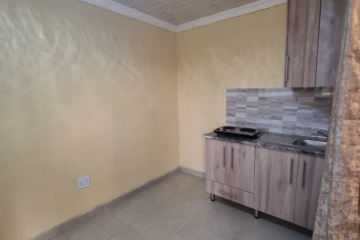 A compact kitchen area featuring built-in cabinetry, a stainless steel sink, an electric cooktop, and tiled flooring.