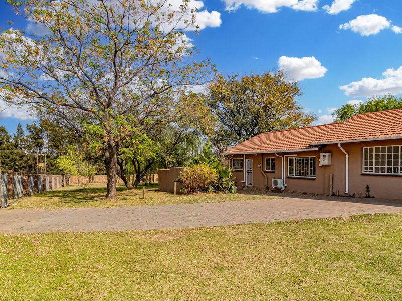 Rear view of the cottage featuring a paved driveway, established garden, terracotta roof tiles, and secure perimeter fencing.