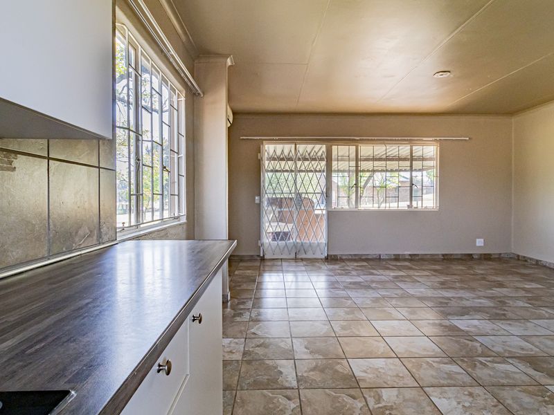 Spacious open-plan living area featuring tiled flooring, kitchen cabinetry with laminate countertops, and secure access via a security gate.