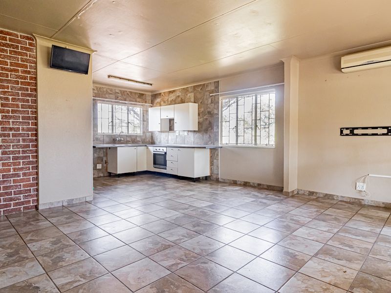 Spacious open-plan living and kitchen area featuring tiled flooring, an exposed brick accent wall, and functional built-in cabinetry with integrated oven and hob.