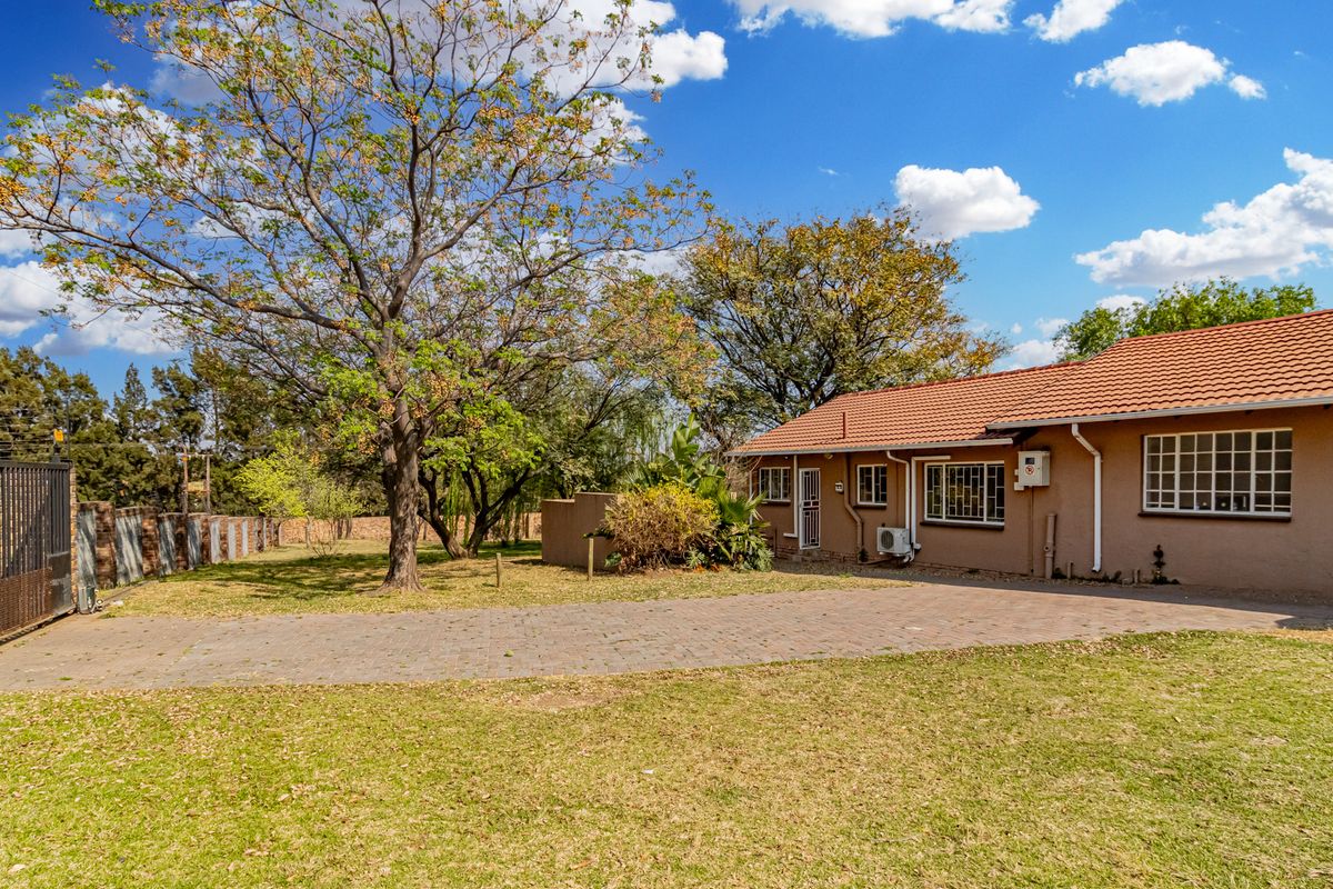 Rear view of the cottage featuring a paved driveway, established garden, terracotta roof tiles, and secure perimeter fencing.