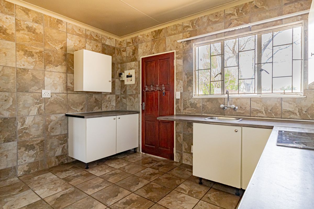 A functional kitchen featuring tiled walls and floors, built-in cabinetry, laminate countertops, and an integrated electric hob with a window view.
