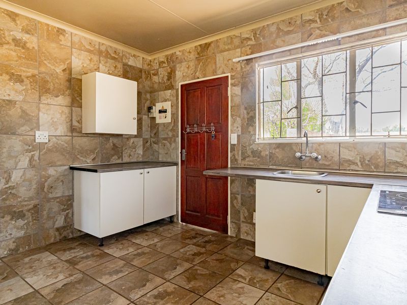A functional kitchen featuring tiled walls and floors, built-in cabinetry, laminate countertops, and an integrated electric hob with a window view.