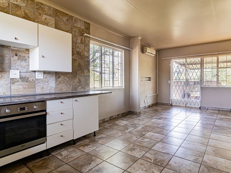 Open-plan kitchen and living area featuring tiled flooring, built-in oven, hob, and direct access to an outdoor patio through a security-fitted sliding door.