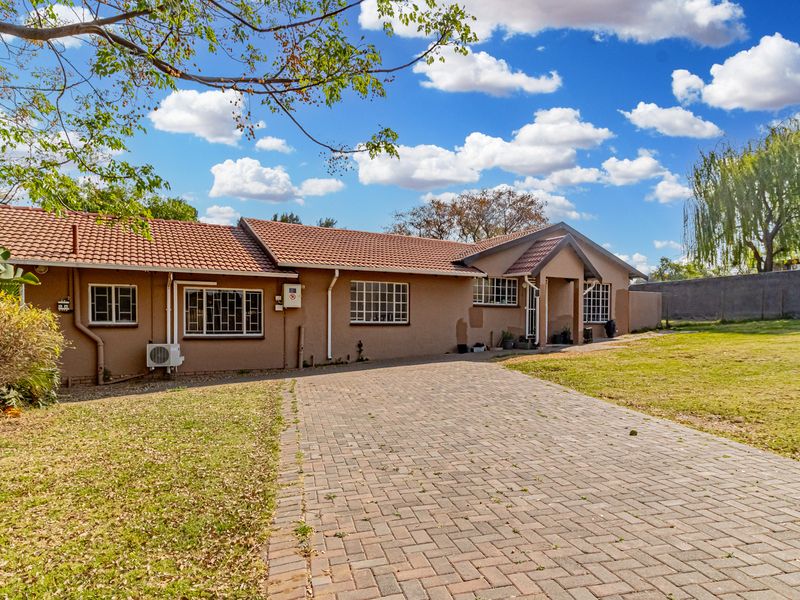 Front view of a cottage featuring a tiled roof, brick paved driveway, and security bars on windows, set on a spacious lawned plot.
