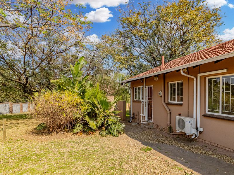 Rear view of the cottage featuring a tiled roof, security bars on windows, an external air conditioning unit, and a paved walkway leading to the garden.