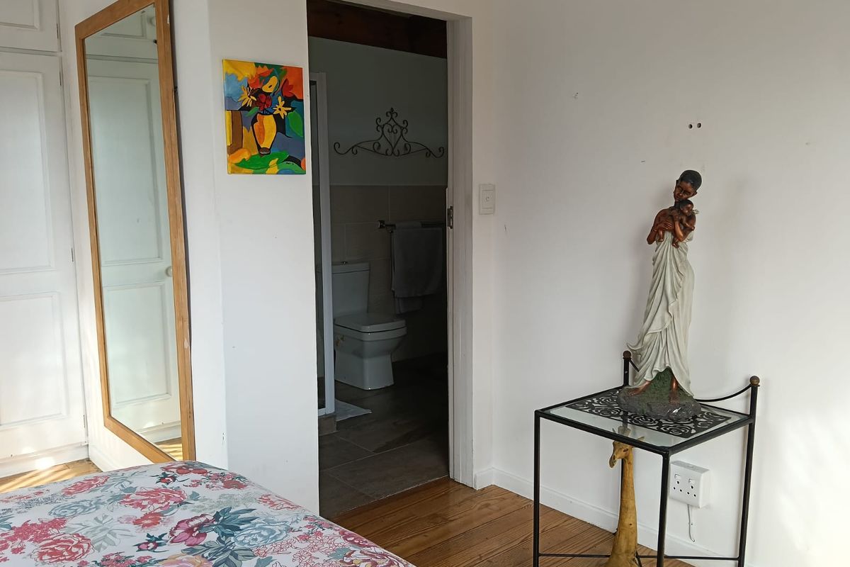 A bedroom interior featuring polished timber flooring and a doorway leading into an adjoining bathroom with tiled flooring.