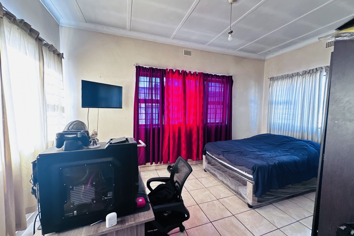 A bedroom featuring tiled flooring, large windows with security bars, and a simple ceiling finish.