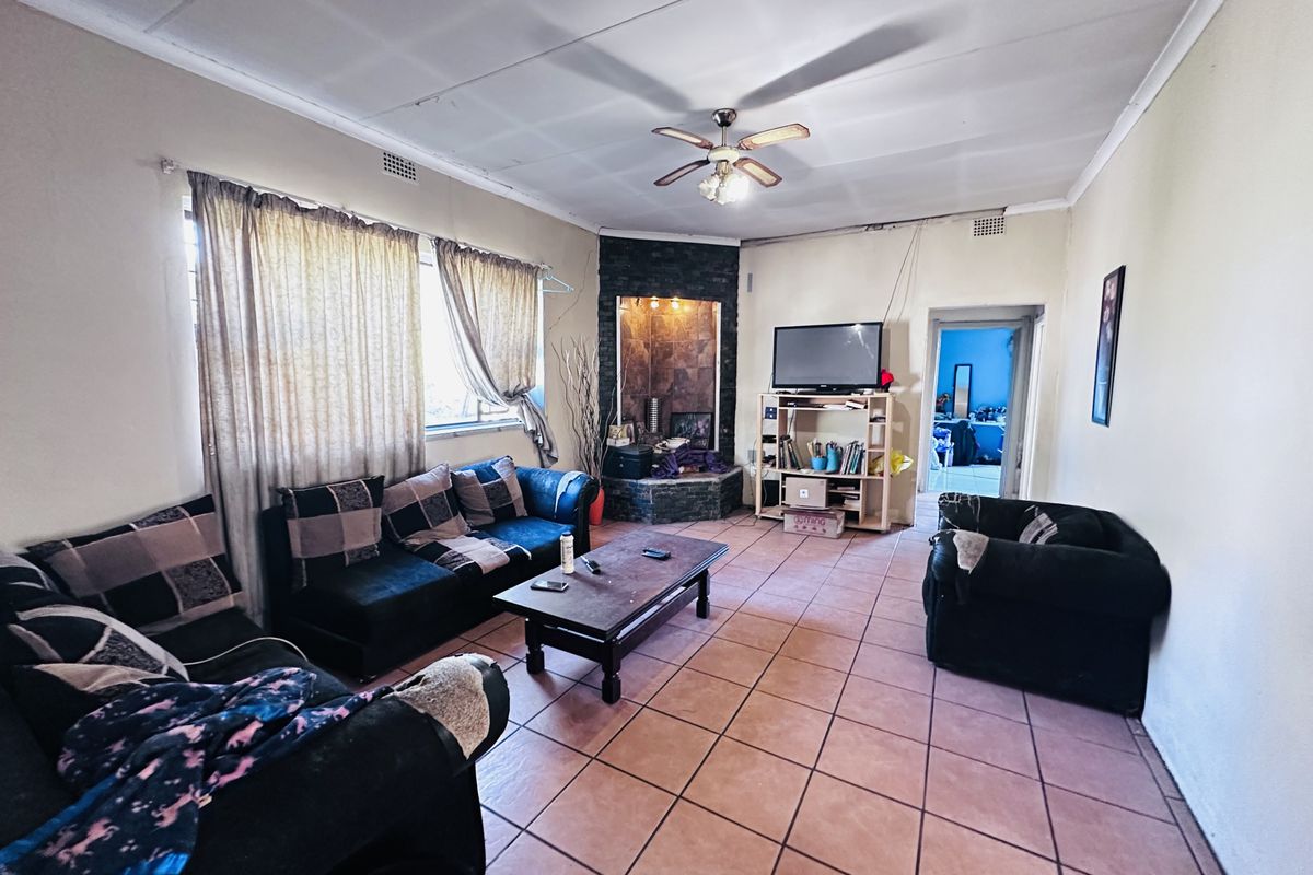 A spacious living room featuring tiled flooring, a built-in corner fireplace with stone cladding, and a ceiling fan.