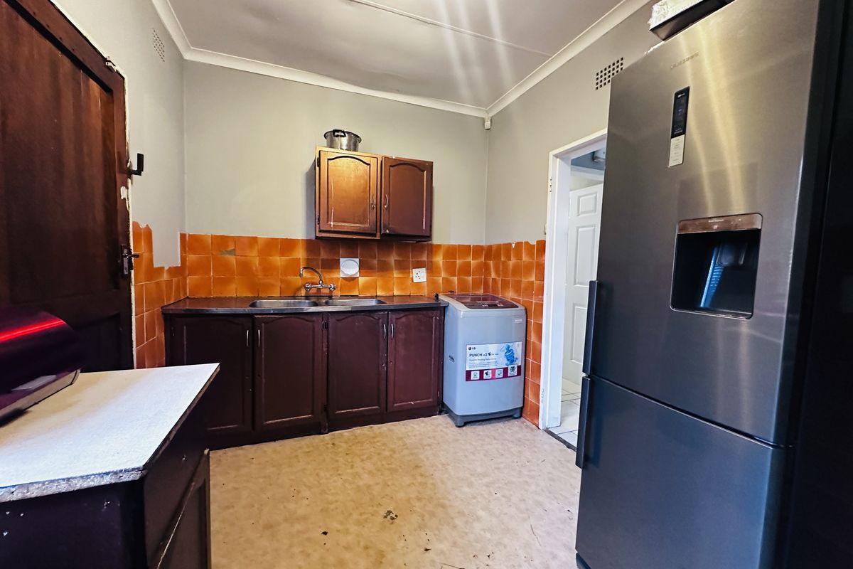 A functional kitchen space featuring dark wood cabinetry, a stainless steel sink, and orange tiled splashbacks, requiring cosmetic updates to improve its overall condition.