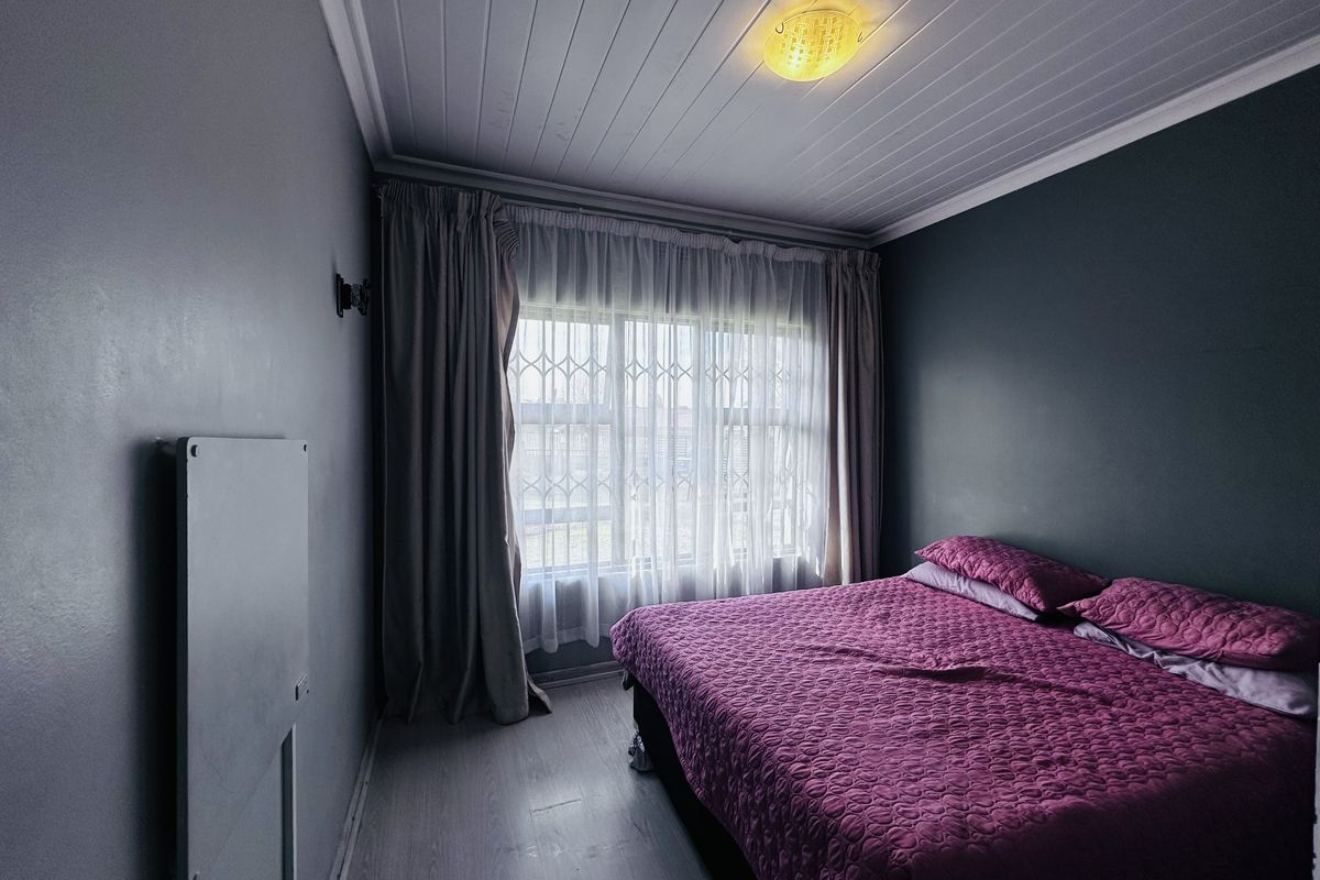 A bedroom featuring timber-look laminate flooring, a tongue-and-groove ceiling, and a window fitted with a security gate.