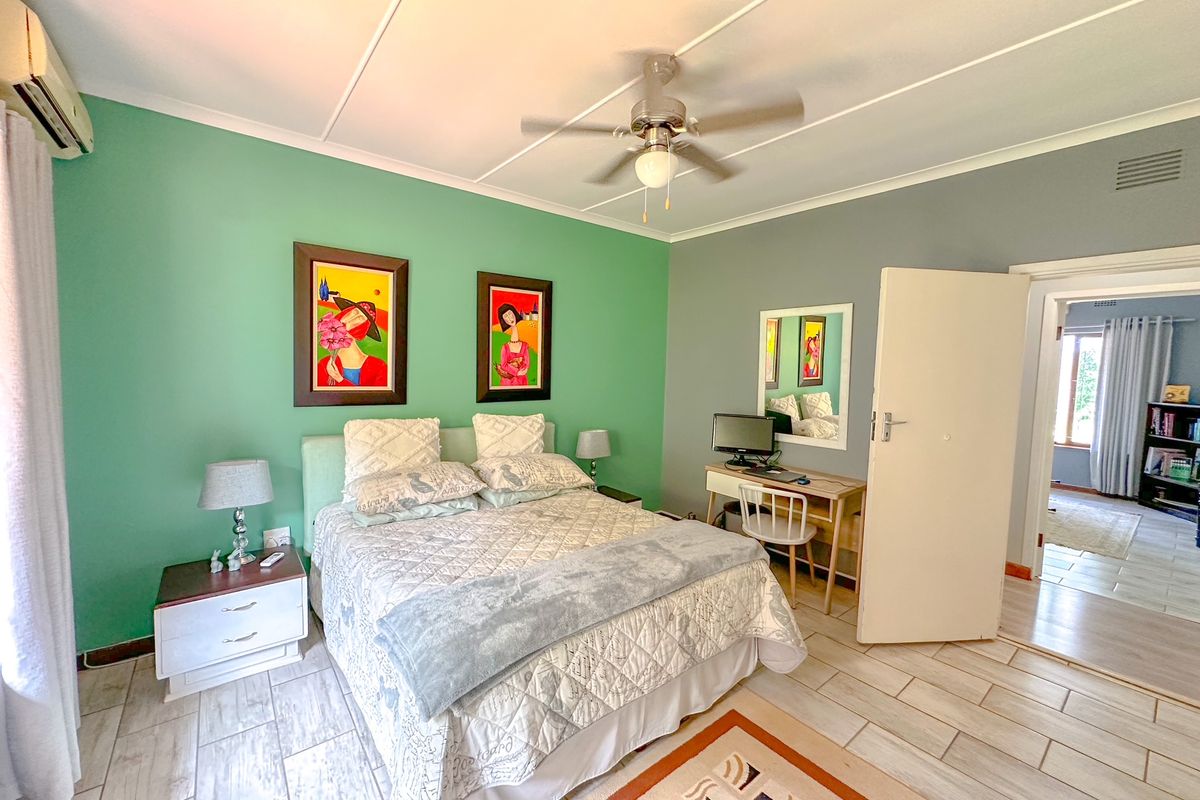 A well-lit bedroom featuring a ceiling fan, split-system air conditioning unit, and tiled flooring, with an open doorway leading to an adjacent room.
