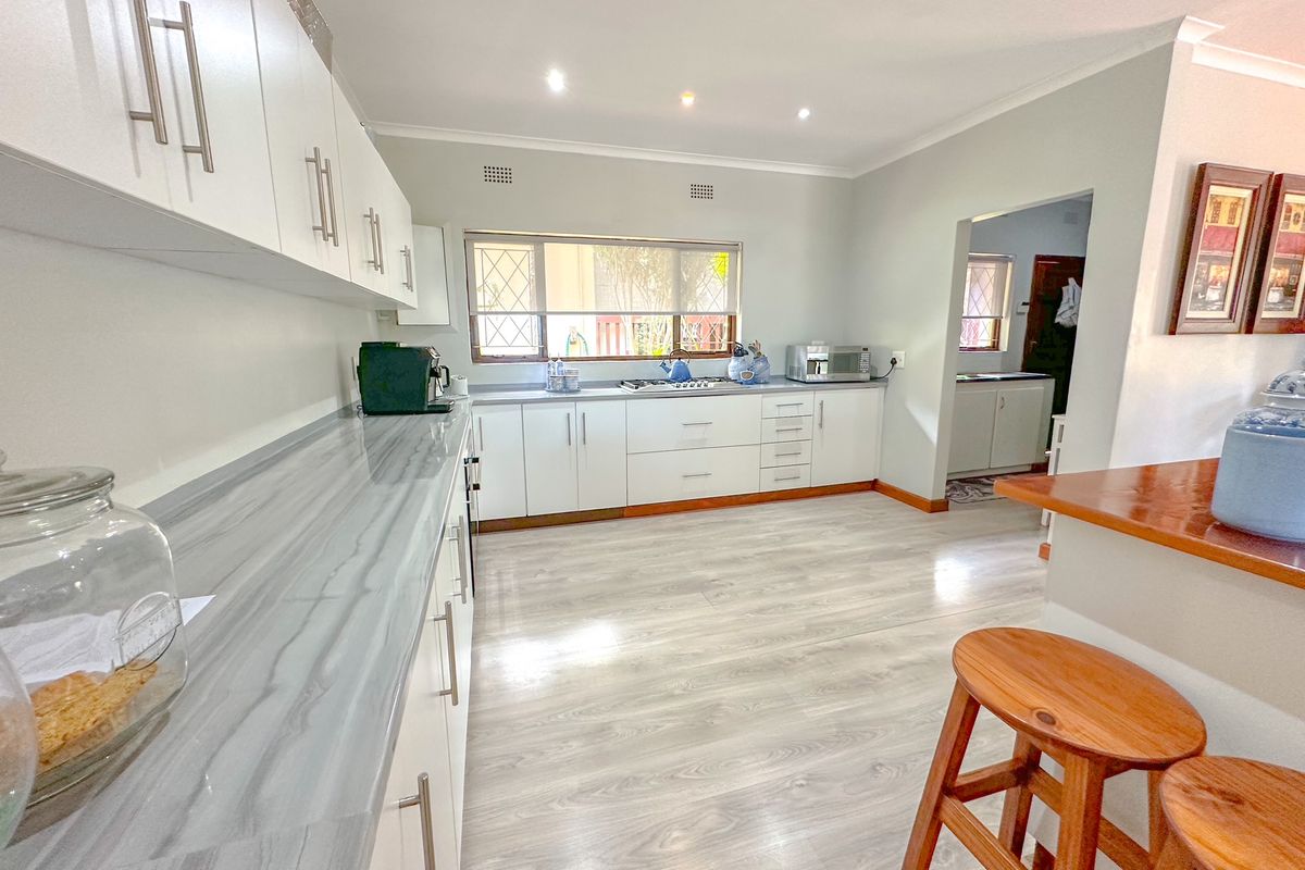 A bright, modern kitchen featuring white cabinetry, stone-look countertops, recessed lighting, and light wood-look flooring, with an adjacent scullery area.