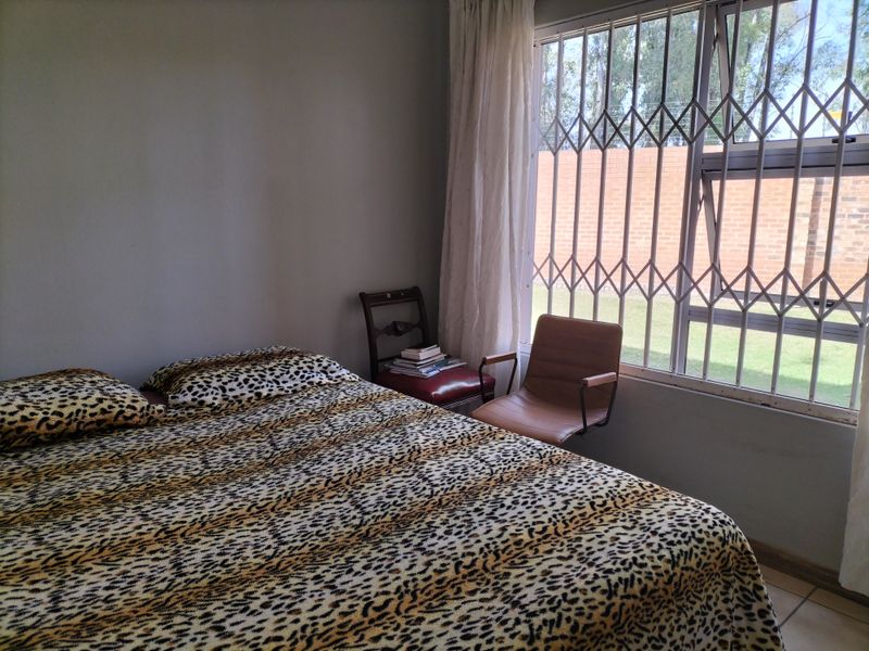 A bedroom featuring tiled flooring and a window fitted with a security gate, offering a view of the exterior brick wall.