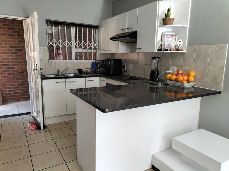Functional kitchen featuring granite countertops, white cabinetry, a double sink, and a tiled backsplash, with direct access to an exterior area.