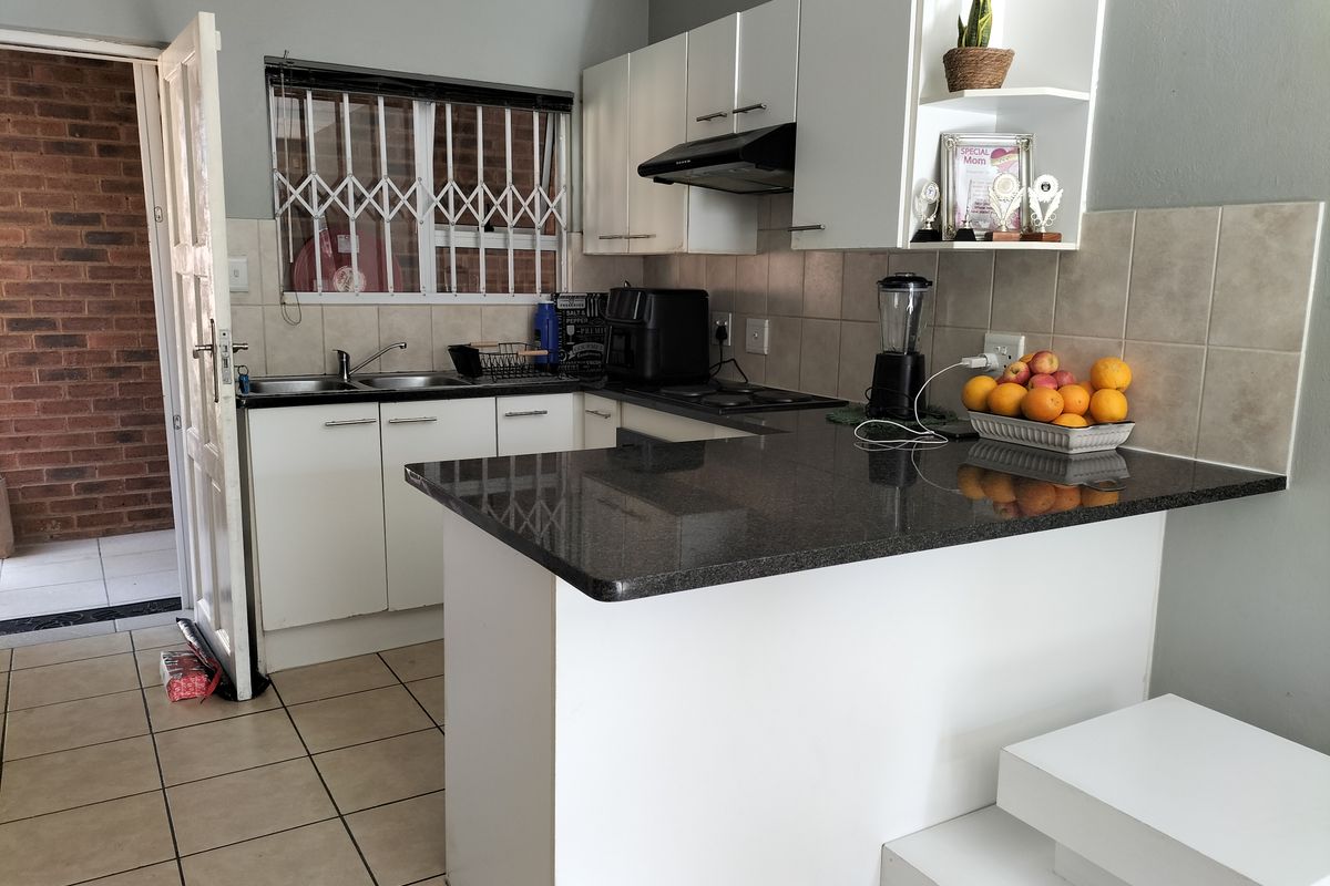 Functional kitchen featuring granite countertops, white cabinetry, a double sink, and a tiled backsplash, with direct access to an exterior area.