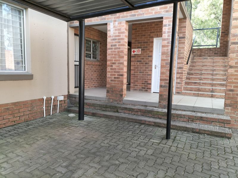 Front exterior view of the townhouse featuring a covered carport, paved driveway, and an external staircase leading to the upper level.