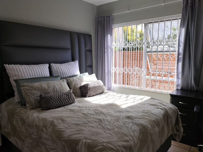 A well-lit bedroom featuring a window with a fitted security gate and neutral wall finishes.