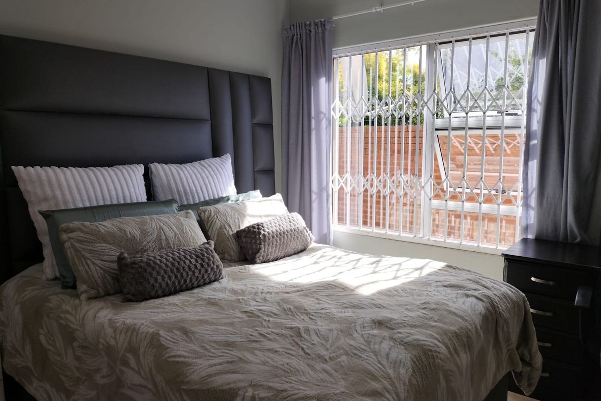 A well-lit bedroom featuring a window with a fitted security gate and neutral wall finishes.