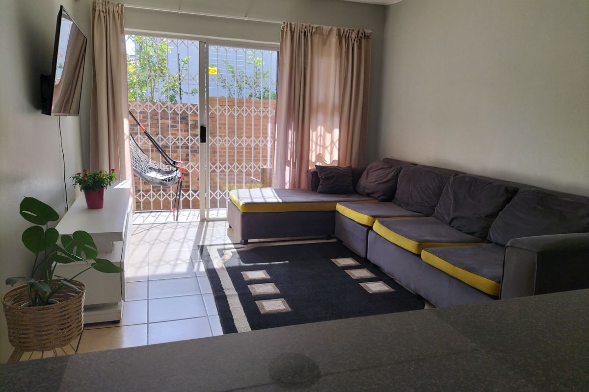 A living room featuring tiled flooring and a sliding glass door with a security gate leading to an outdoor area.