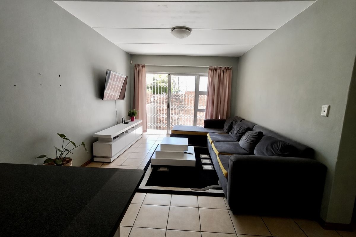 A living room featuring tiled flooring and a sliding glass door with a security gate, providing access to the exterior.
