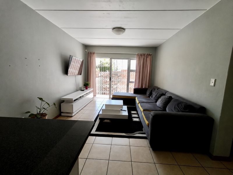 A living room featuring tiled flooring and a sliding glass door with a security gate, providing access to the exterior.
