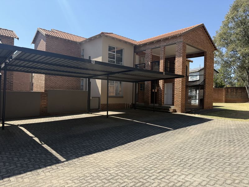 Front view of a multi-story townhouse featuring a brick facade, tiled roof, covered carport, and paved driveway area.