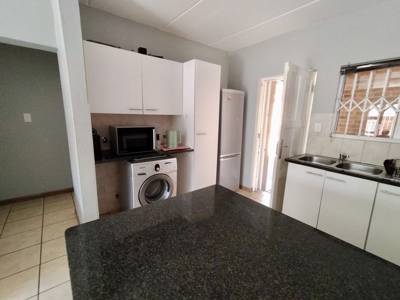 Functional kitchen featuring granite countertops, white cabinetry, double basin sink, and tiled flooring with a window security gate.