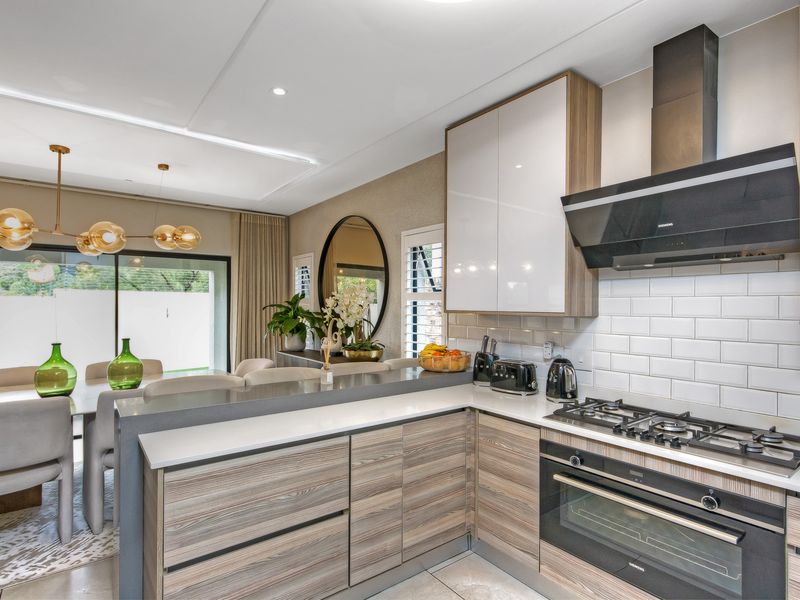 Modern open-plan kitchen featuring sleek wood-finish cabinetry, quartz countertops, subway tile backsplash, and integrated gas appliances, flowing into a bright dining area.