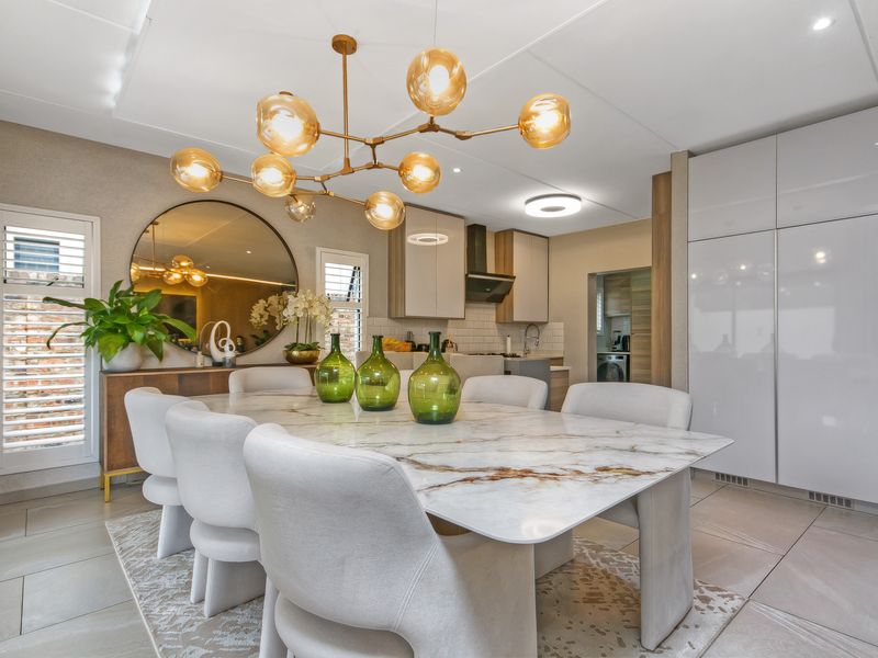 Modern open-plan dining and kitchen area featuring sleek cabinetry, high-end finishes, tiled flooring, and contemporary lighting fixtures.