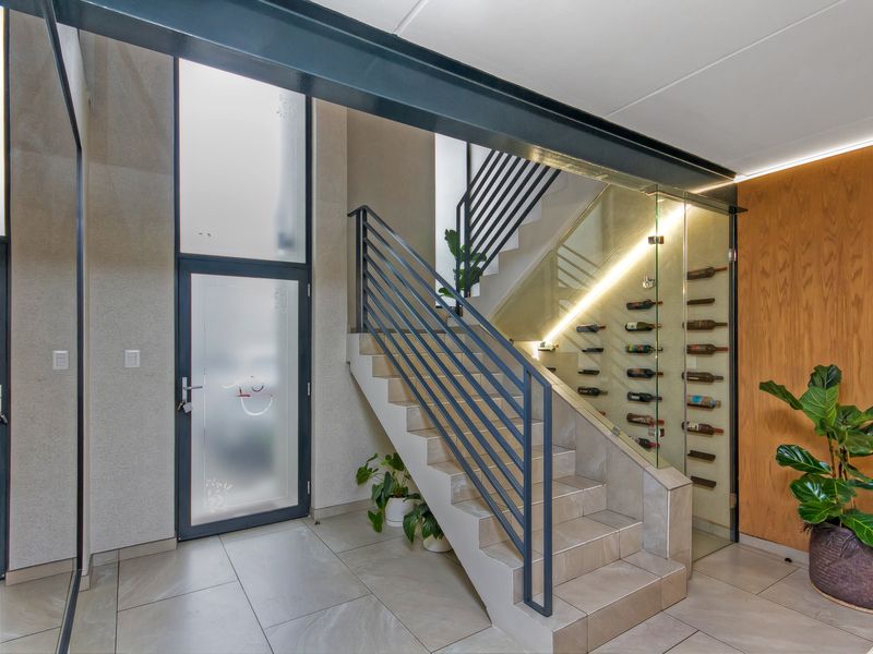 Modern entrance foyer featuring a tiled staircase with metal balustrades and a sleek, glass-enclosed wine storage display.