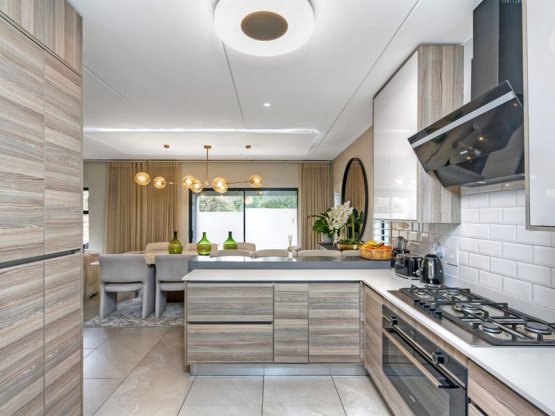 Modern open-plan kitchen and dining area featuring contemporary wood-grain cabinetry, integrated appliances, stone countertops, and seamless flow to the outdoor patio.