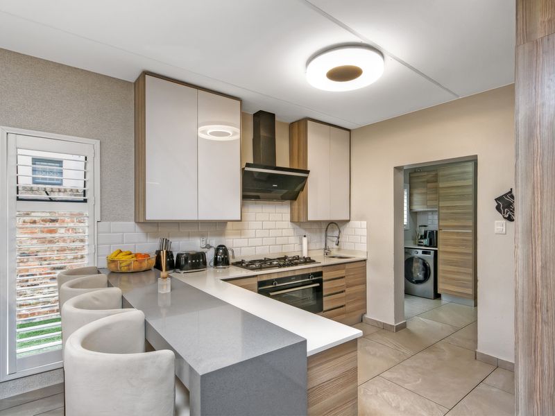 Modern kitchen featuring stone countertops, a gas hob, built-in oven, subway tile backsplash, and a breakfast bar, with an adjacent scullery area.
