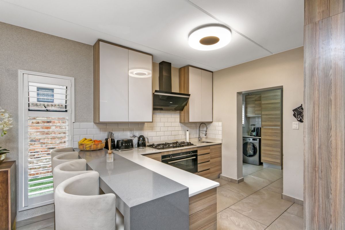 Modern kitchen featuring stone countertops, a gas hob, built-in oven, subway tile backsplash, and a breakfast bar, with an adjacent scullery area.