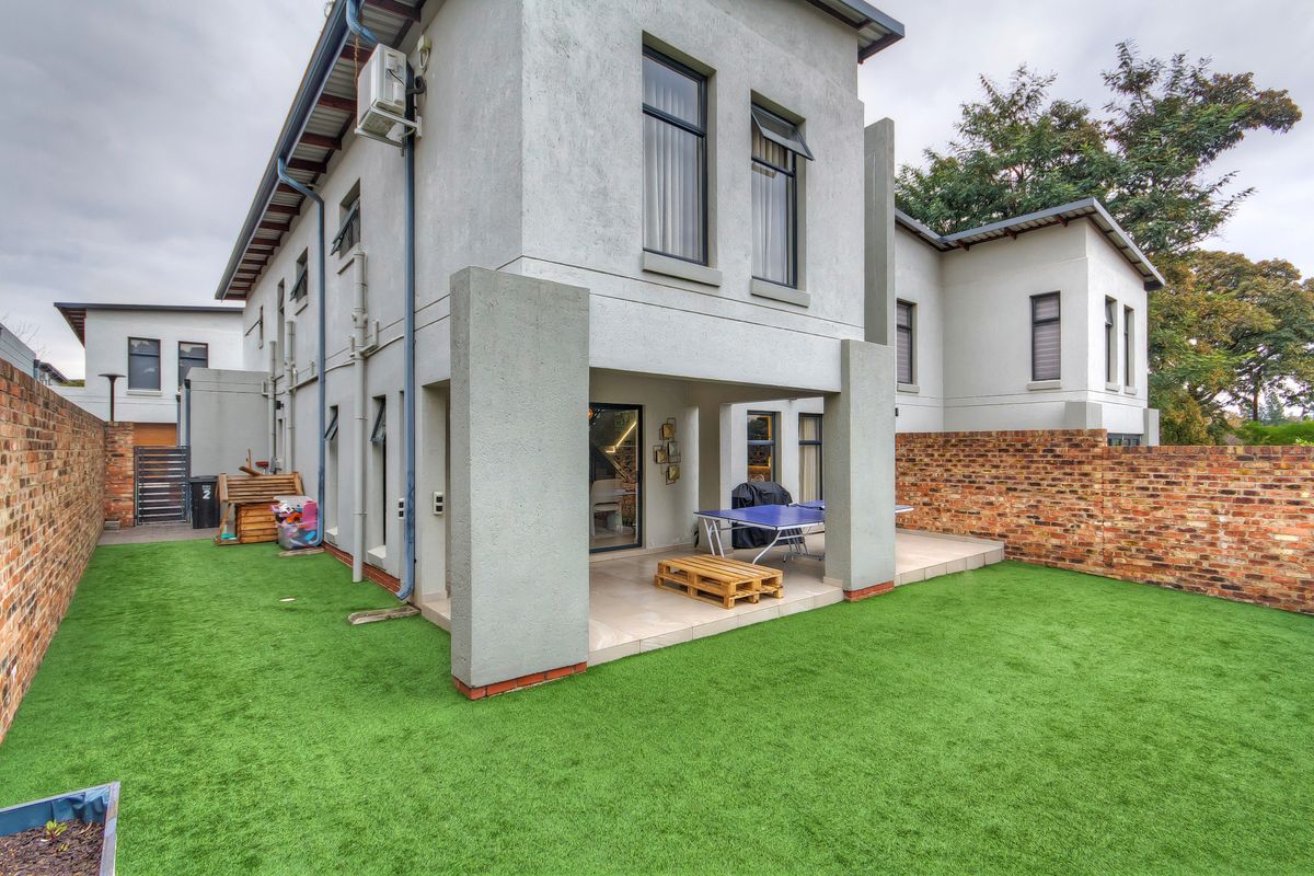 Rear view of the townhouse featuring a covered patio with tiled flooring, artificial lawn, and a secure brick boundary wall.