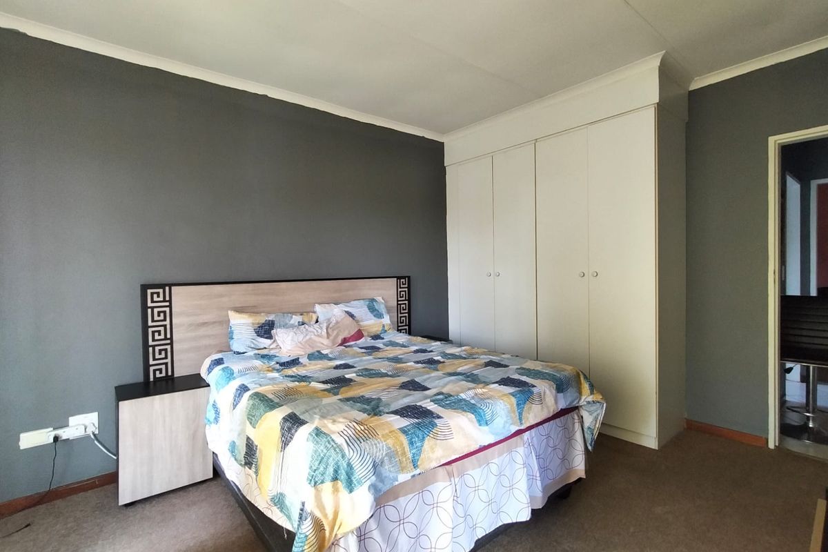 A bedroom featuring built-in cupboards and a neutral grey accent wall, providing functional storage and a comfortable layout.