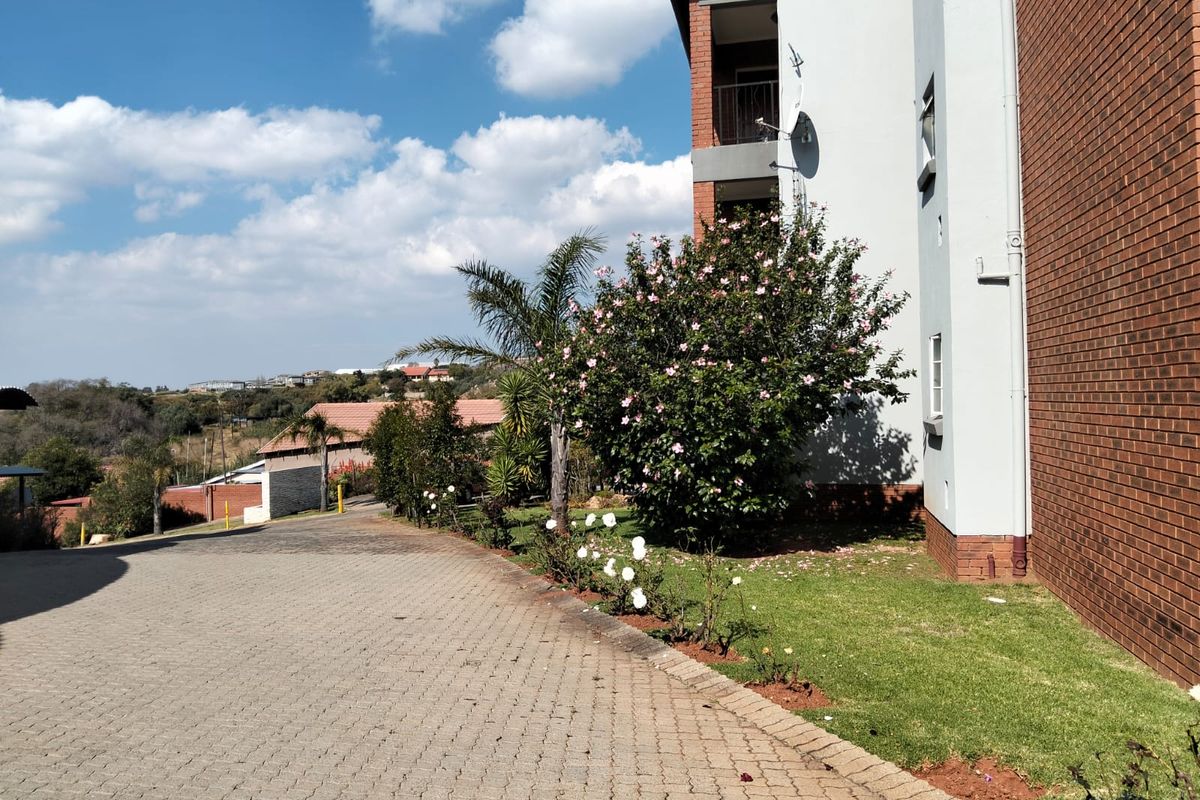 Exterior view of the apartment building featuring brick and rendered facade, paved driveway, and landscaped garden area.