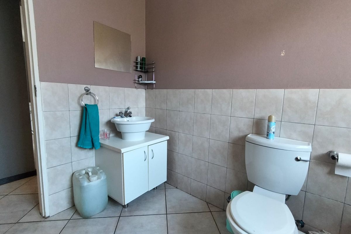 A functional bathroom featuring a pedestal-style vanity with basin, a standard toilet, and neutral wall and floor tiling.