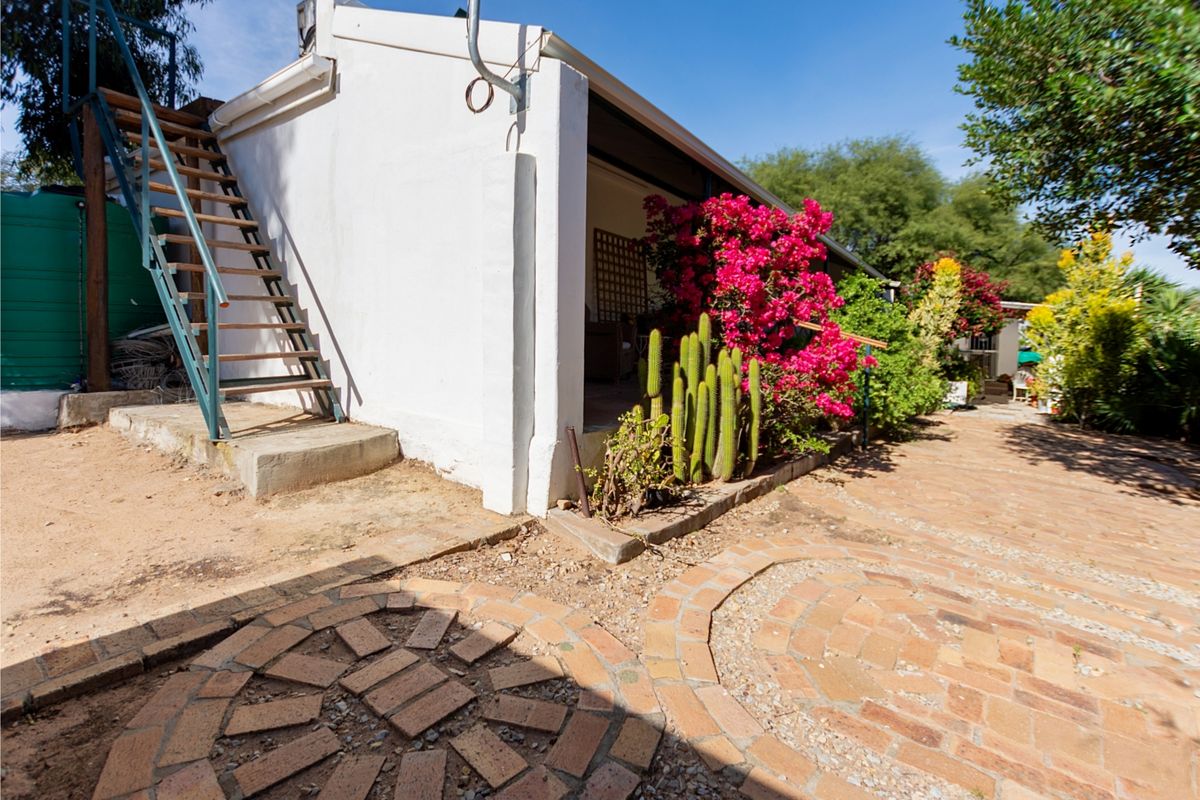 Rear exterior view featuring a covered patio, brick paved courtyard, and an external staircase leading to an upper level.