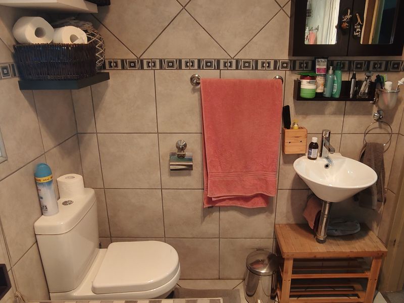 A functional bathroom featuring ceramic wall tiles, a pedestal washbasin with chrome mixer, and a standard toilet.