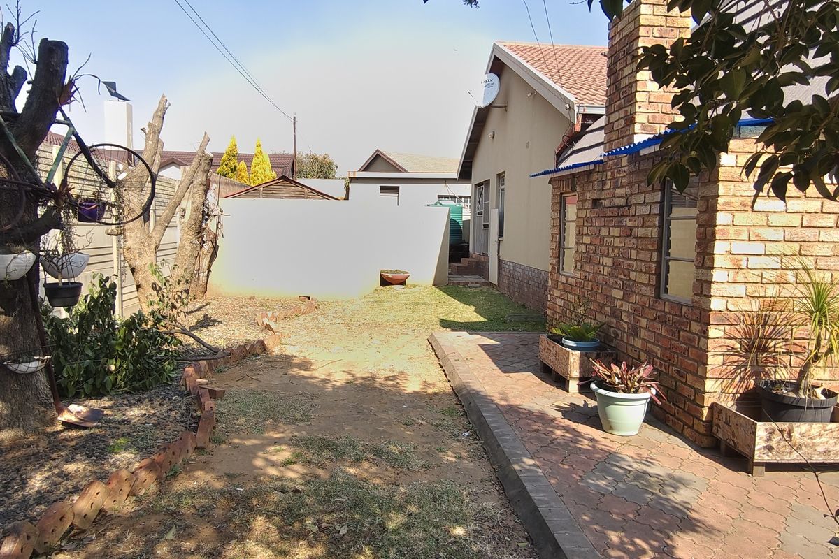 A rear garden view featuring a brick chimney, paved patio area, and boundary wall, providing a functional outdoor space for the property.