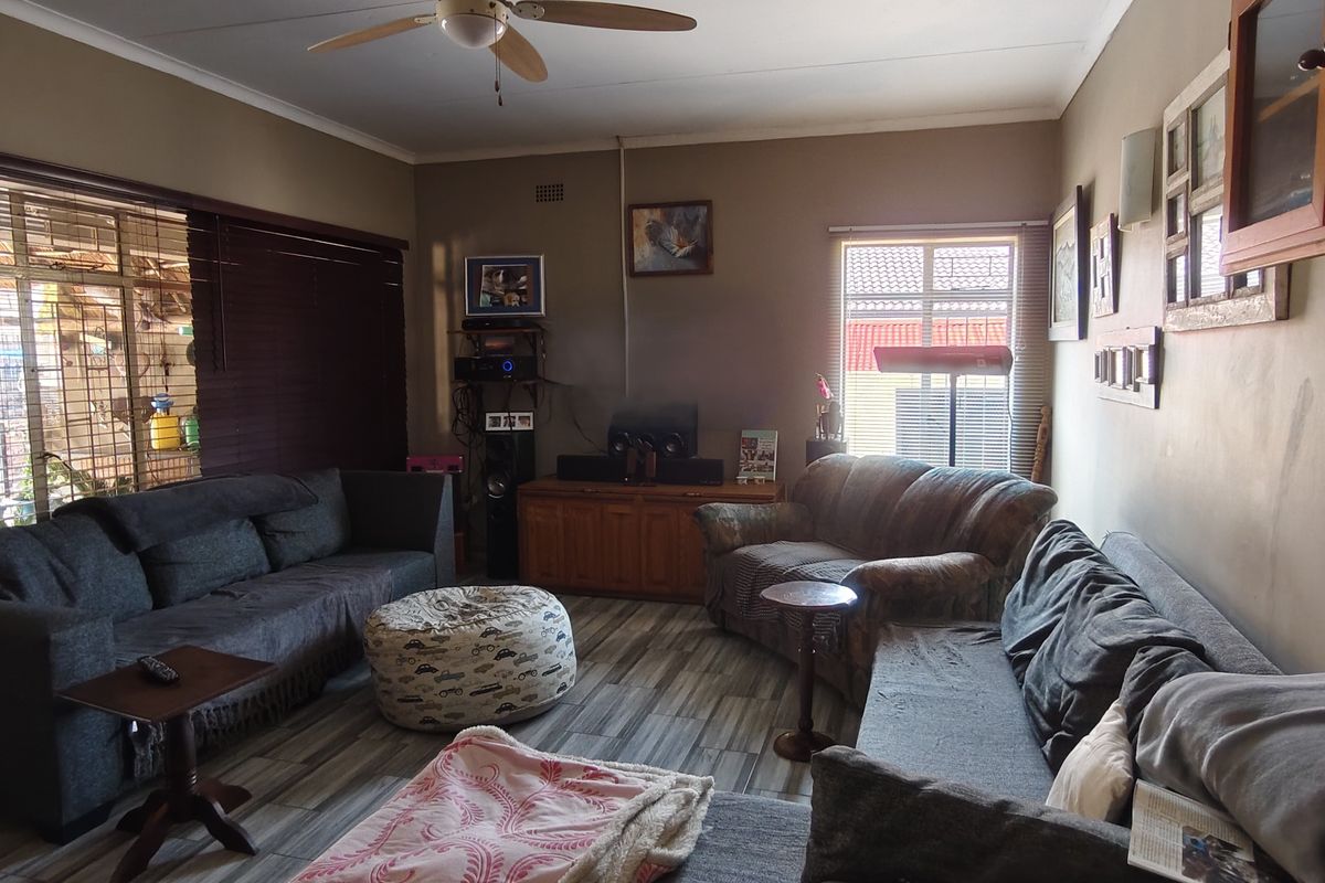 A living room featuring laminate flooring, a ceiling fan, and large windows with venetian blinds, offering a functional and lived-in space.