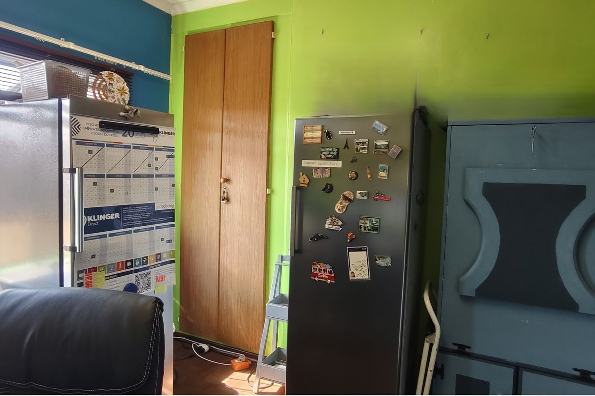 A kitchen area featuring a built-in wooden cupboard and large window, currently used for storage and workspace.
