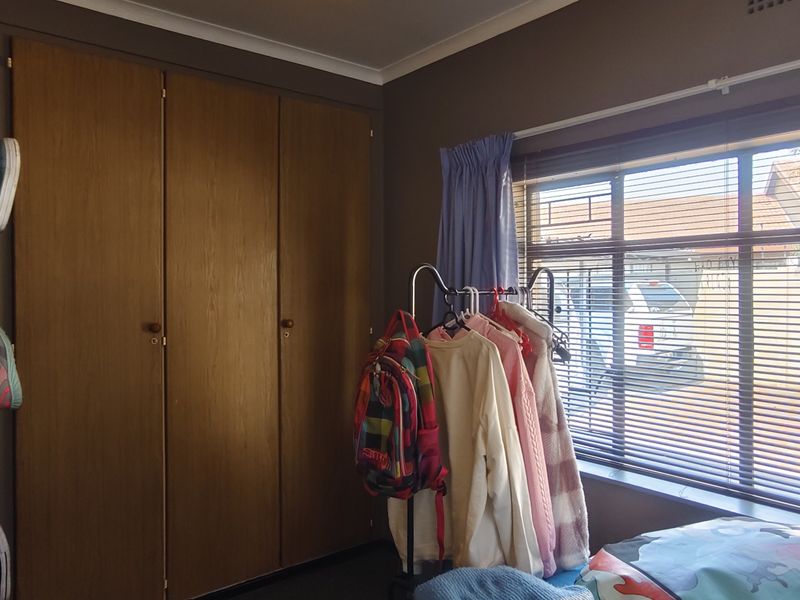 A bedroom featuring built-in wooden cupboards and a large window allowing natural light, providing a functional space with standard finishes.