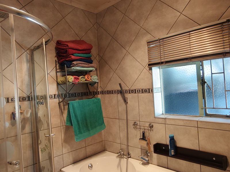 A functional bathroom featuring a shower enclosure, bathtub, tiled walls, and a window with security bars and blinds.